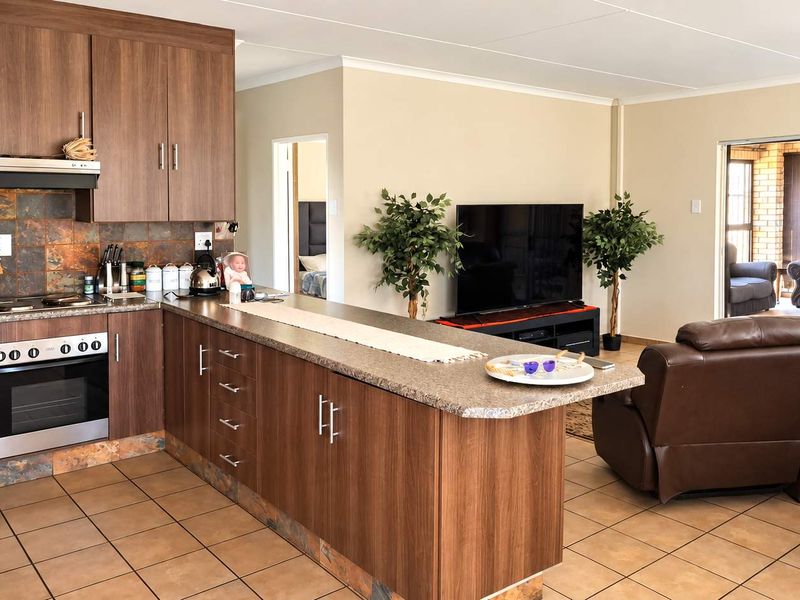 Open-plan living area featuring a functional kitchen with wood-finish cabinetry, stone-look countertops, and tiled flooring, flowing into a comfortable lounge space.