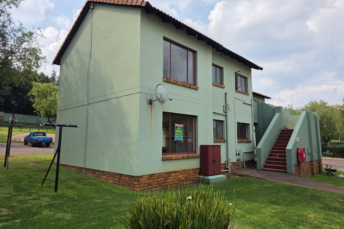 Rear view of a two-story townhouse featuring a tiled roof, external staircase, and brick base, set within a communal garden area.