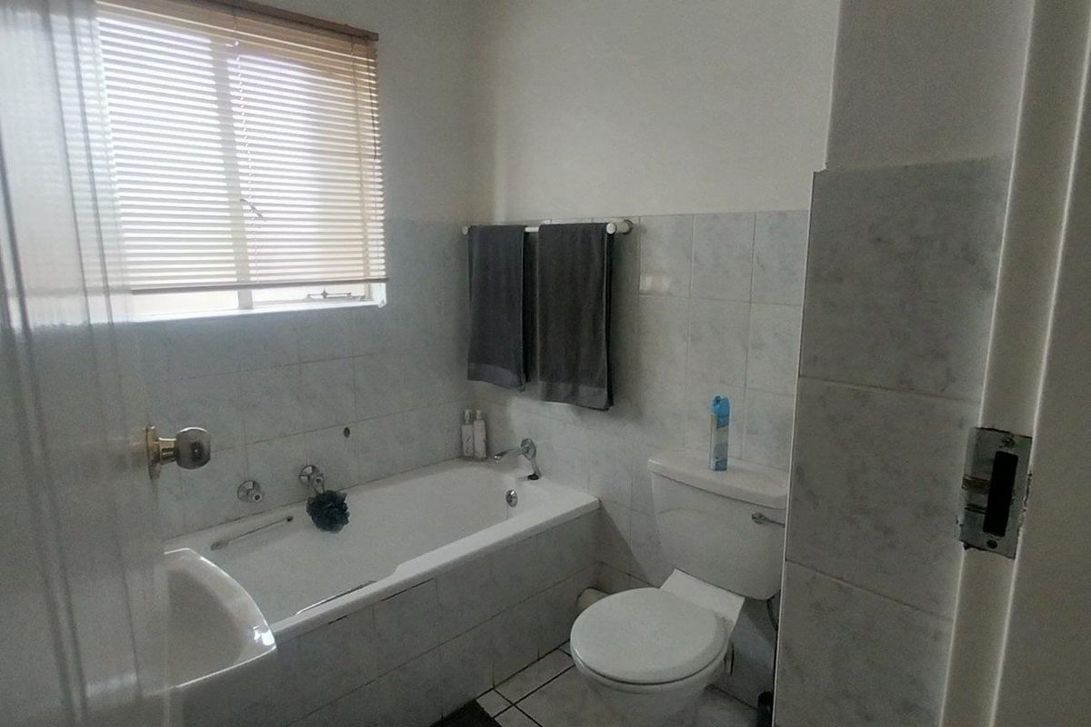 A functional bathroom featuring a built-in bathtub, toilet, and tiled wall finishes with a window providing natural light.