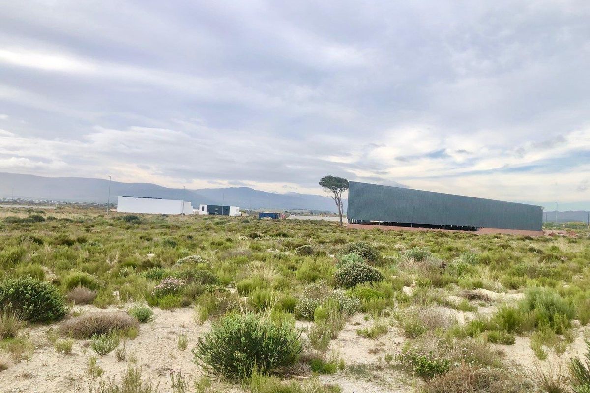 A view of a large commercial warehouse structure situated on a vast, undeveloped plot of land with native vegetation and mountain views.