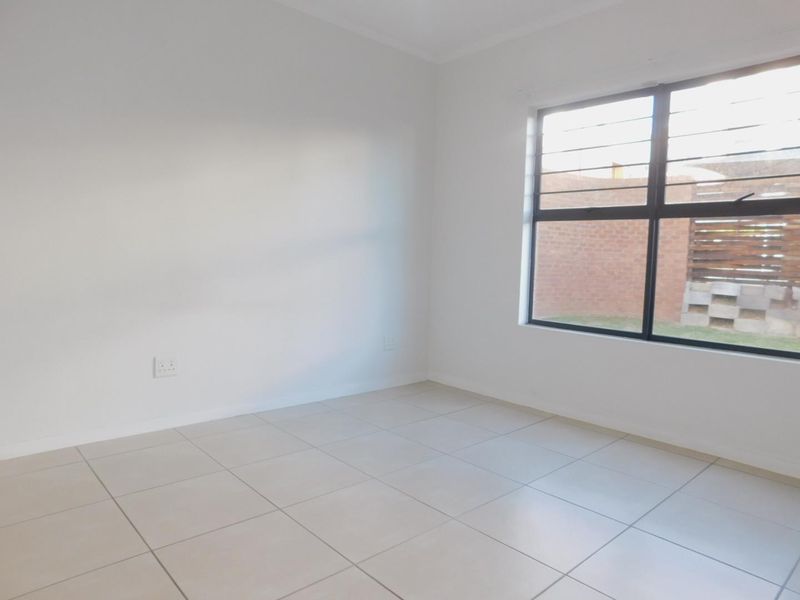 A clean, empty bedroom featuring neutral floor tiles, white walls, and an aluminium-framed window with security bars.