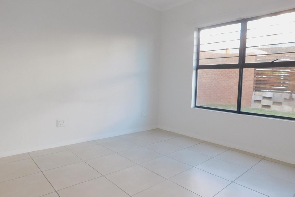 A clean, empty bedroom featuring neutral floor tiles, white walls, and an aluminium-framed window with security bars.