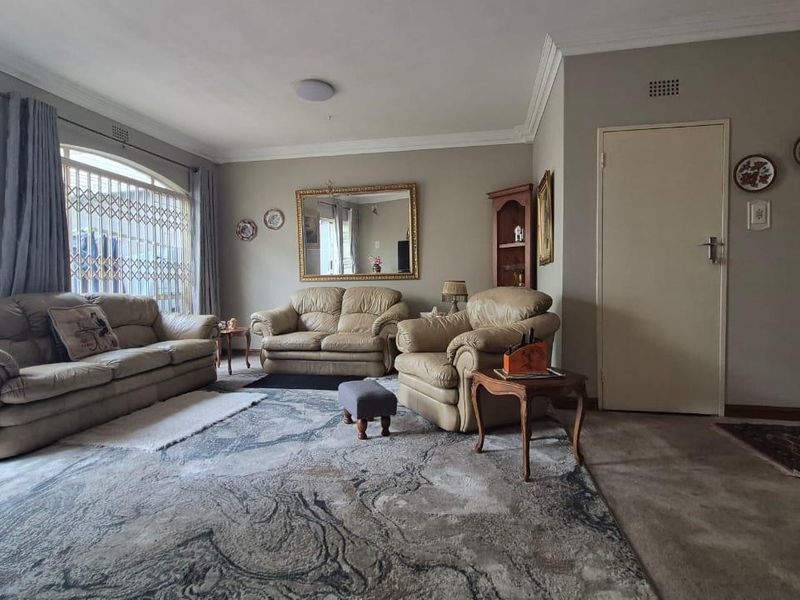 A spacious living room featuring crown molding, neutral wall tones, and a large window with a security gate.
