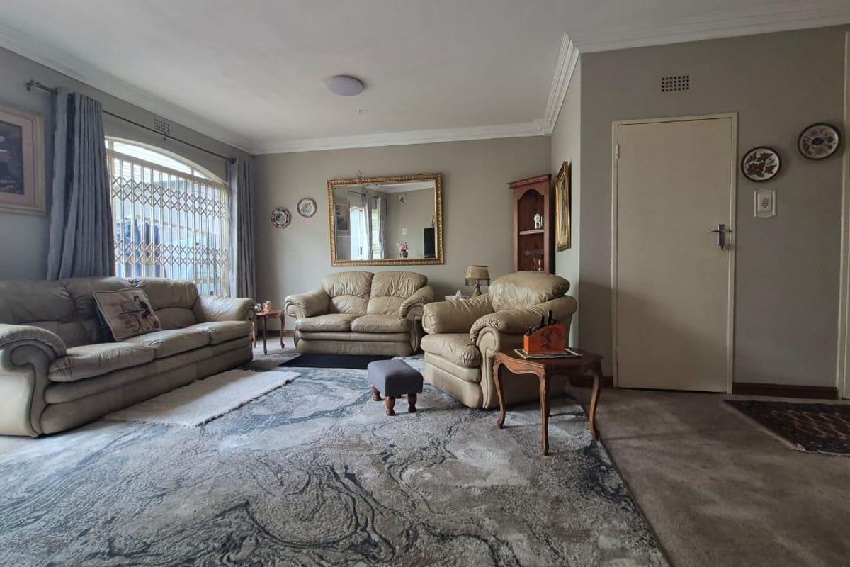 A spacious living room featuring crown molding, neutral wall tones, and a large window with a security gate.