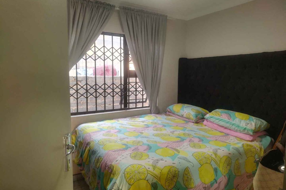 A compact bedroom featuring a window with integrated security bars and neutral wall finishes.