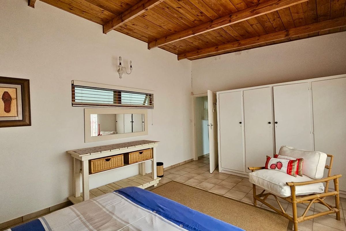 A bedroom featuring a vaulted timber ceiling, built-in wardrobe cabinetry, and tiled flooring, offering a functional and well-lit living space.