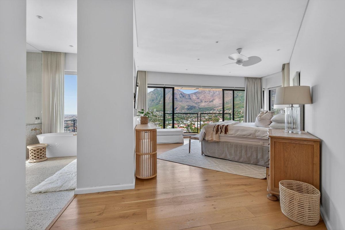 Spacious primary bedroom featuring hardwood floors, an integrated ensuite with a freestanding bathtub, and expansive sliding doors showcasing mountain and city views.