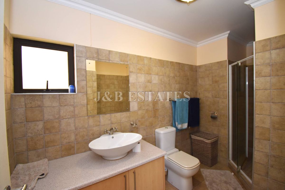 A functional bathroom featuring a vanity with a vessel sink, a toilet, and a glass-enclosed shower with neutral wall tiling.