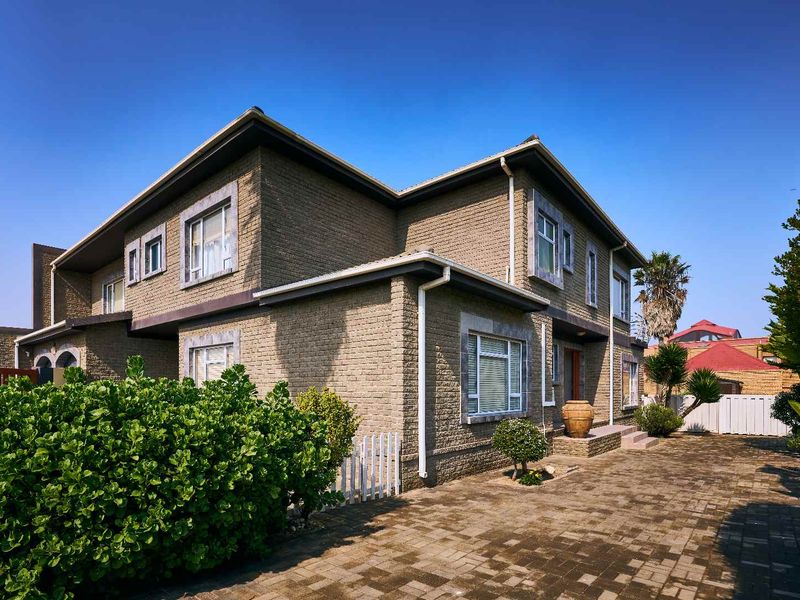 A well-maintained two-story brick house featuring a paved driveway and established garden surroundings.