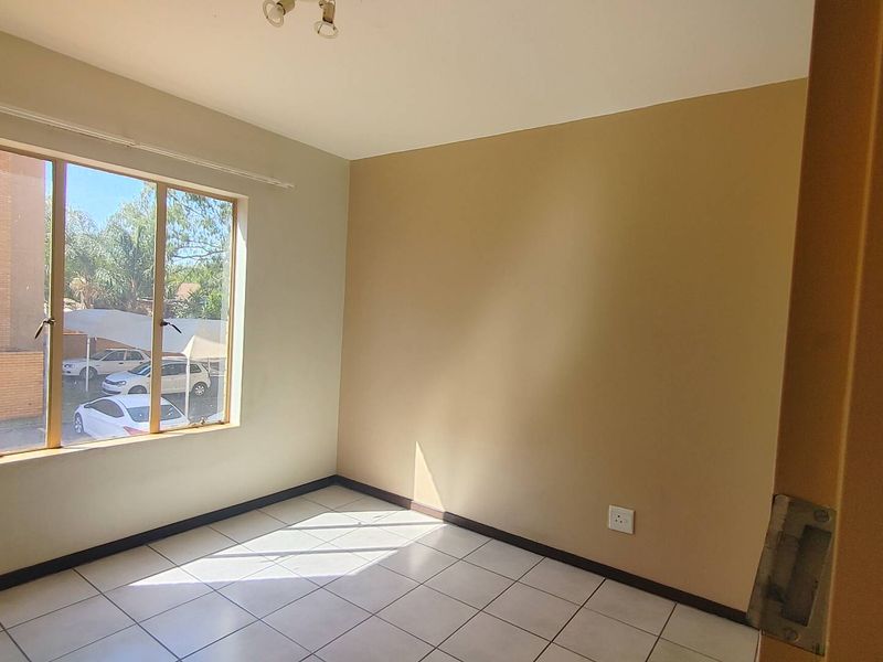 A bright, empty bedroom featuring neutral wall tones, tiled flooring, and a large window providing natural light.
