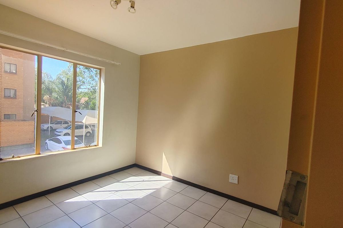 A bright, empty bedroom featuring neutral wall tones, tiled flooring, and a large window providing natural light.