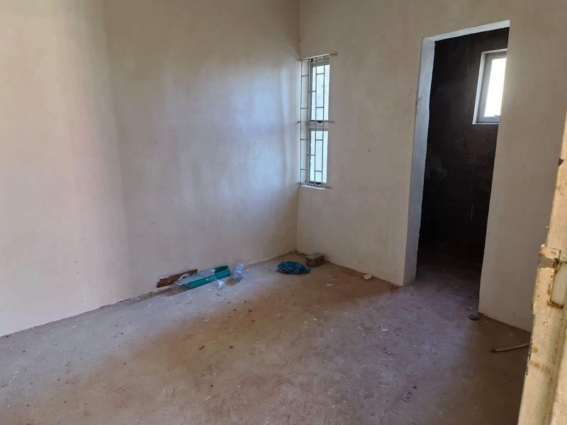 An unfinished bedroom space featuring plastered walls and security bars on the window, currently in a shell condition awaiting final flooring and wall finishes.