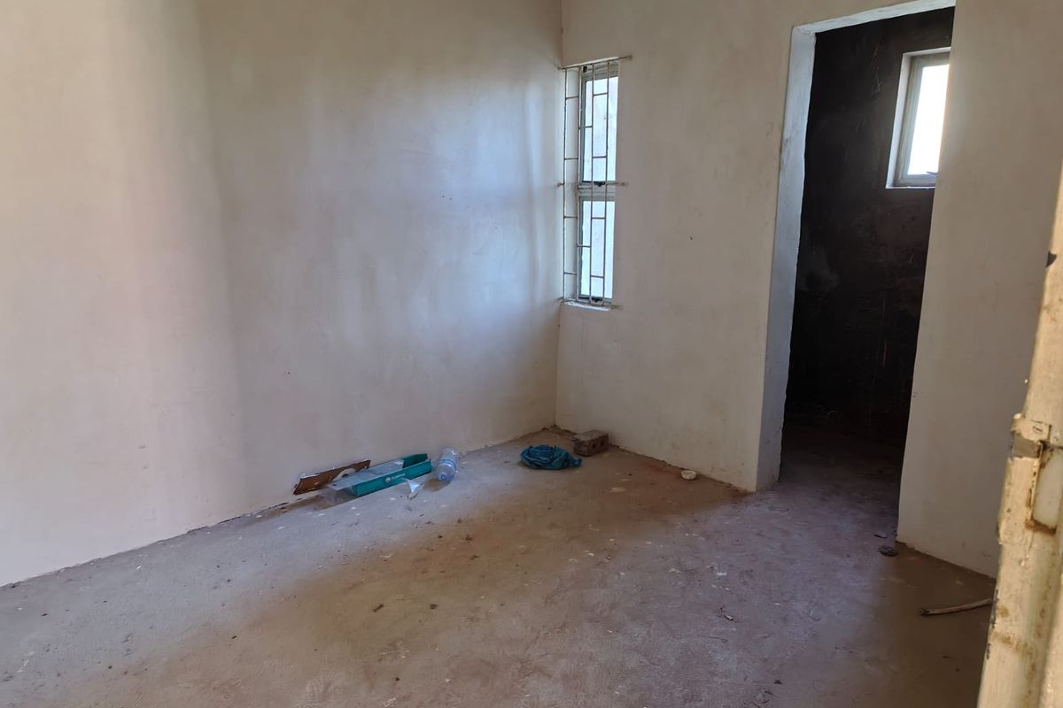 An unfinished bedroom space featuring plastered walls and security bars on the window, currently in a shell condition awaiting final flooring and wall finishes.