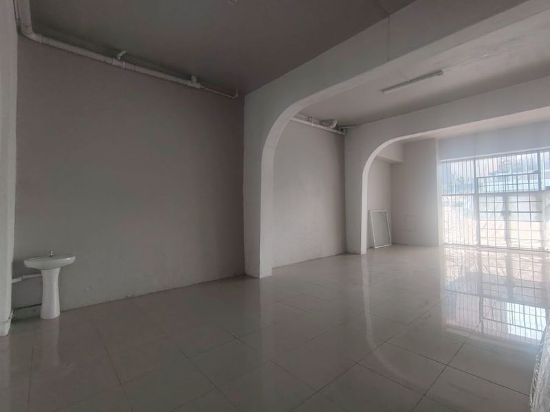 An empty, open-plan commercial space featuring tiled flooring, arched structural details, and a pedestal basin, suitable for various business or retail applications.