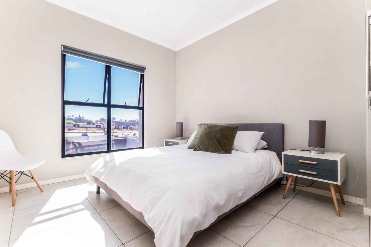 A bright and well-maintained bedroom featuring large windows, neutral wall tones, and tiled flooring.