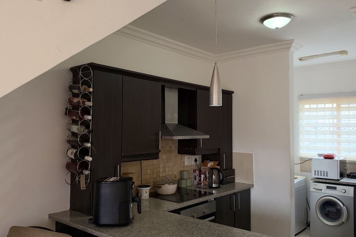 Compact kitchen featuring dark wood cabinetry, granite countertops, built-in oven, and stainless steel extractor fan, with a tiled backsplash and modern pendant lighting.
