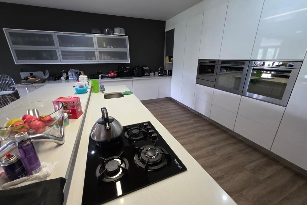 Modern kitchen featuring a large island with a built-in gas hob, integrated wall ovens, and sleek white cabinetry with ample storage space.