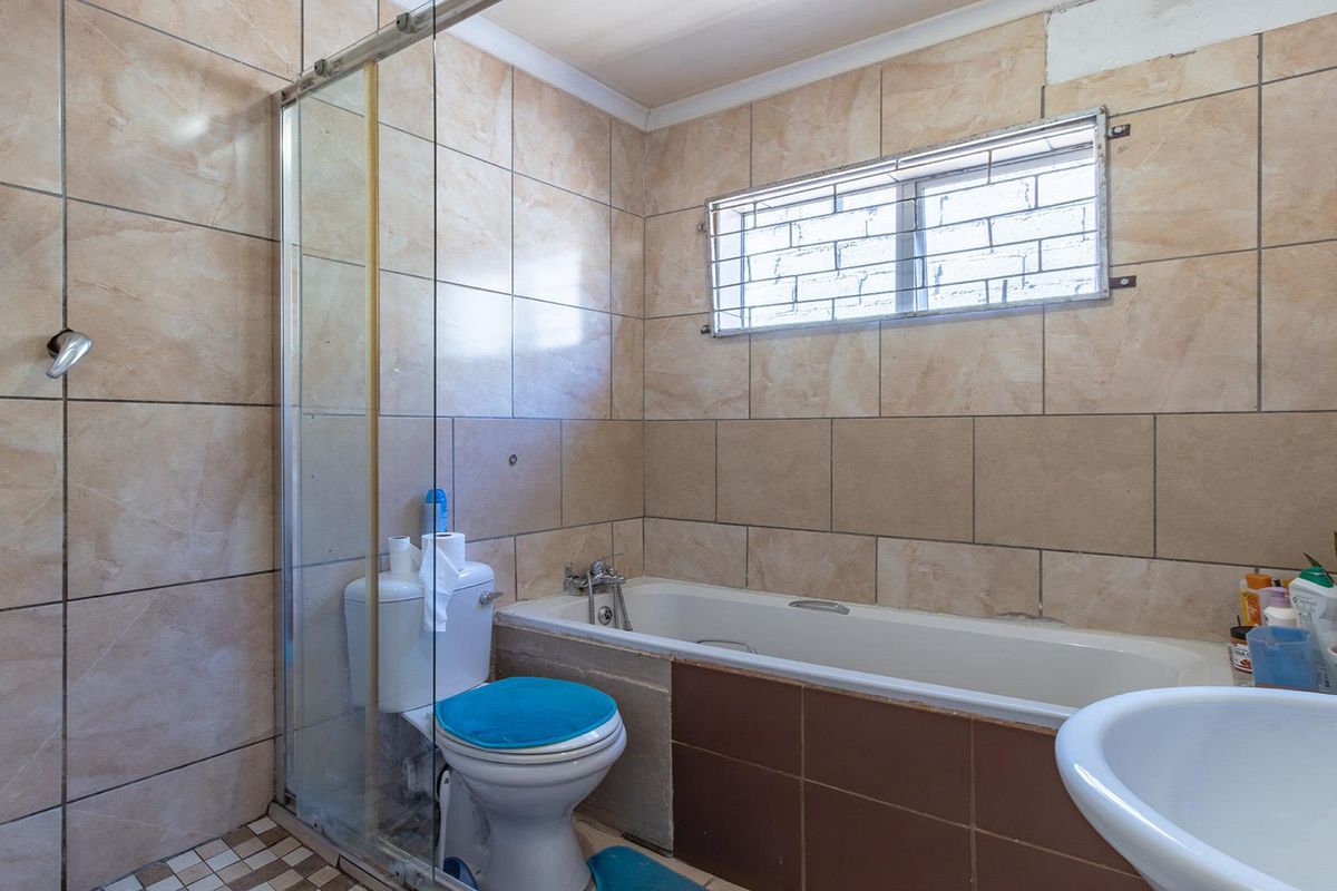 A functional bathroom featuring a shower enclosure, bathtub, toilet, and pedestal basin with neutral wall tiling and a window with security bars.