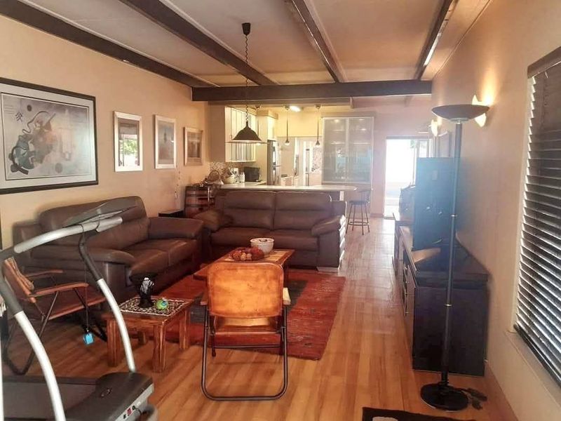 Open-plan living area featuring exposed ceiling beams, laminate flooring, and a connected kitchen with island seating, creating a functional and integrated living space.