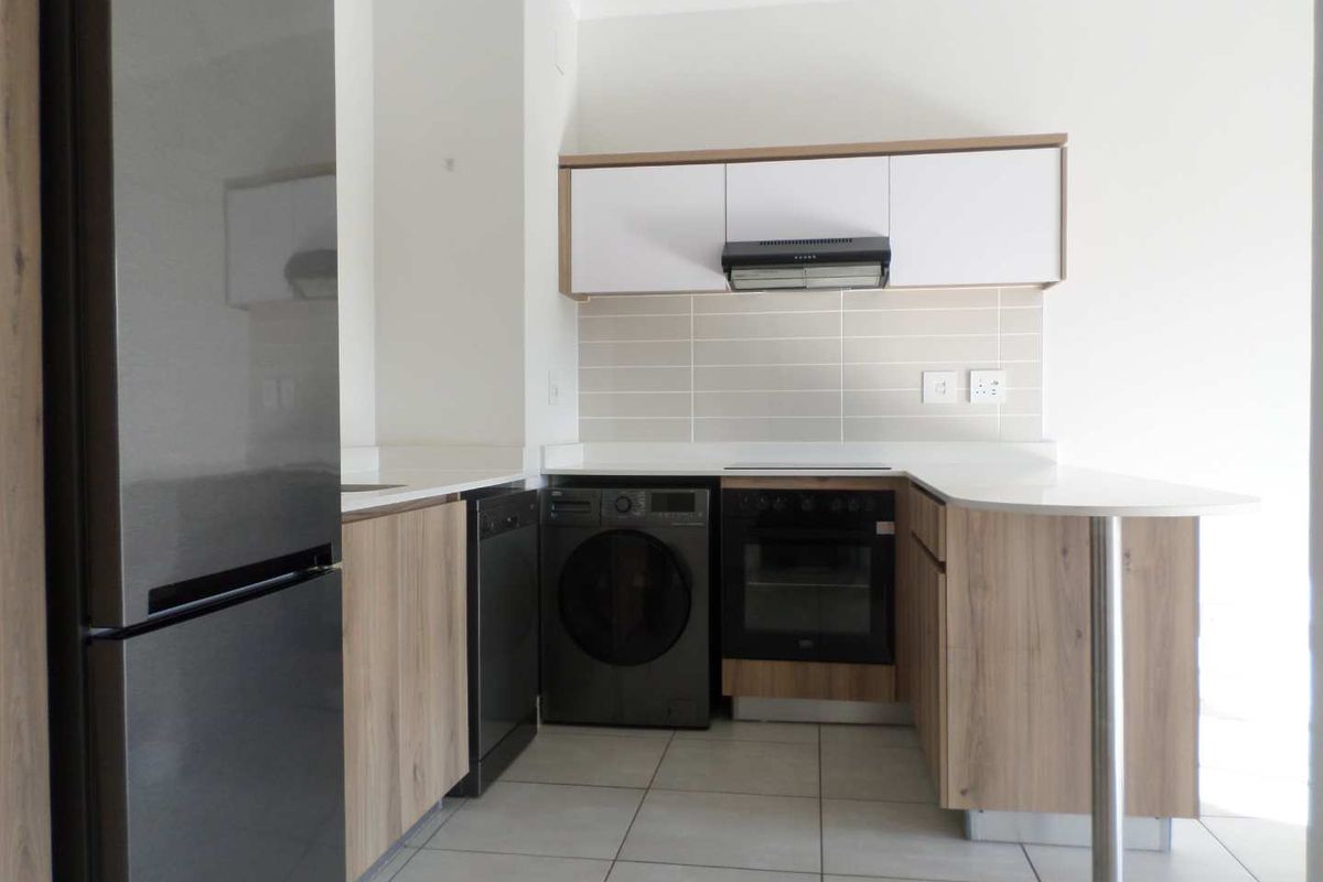 Modern kitchen featuring light wood cabinetry, stone countertops, a tiled backsplash, built-in oven, extractor fan, and a convenient breakfast bar.