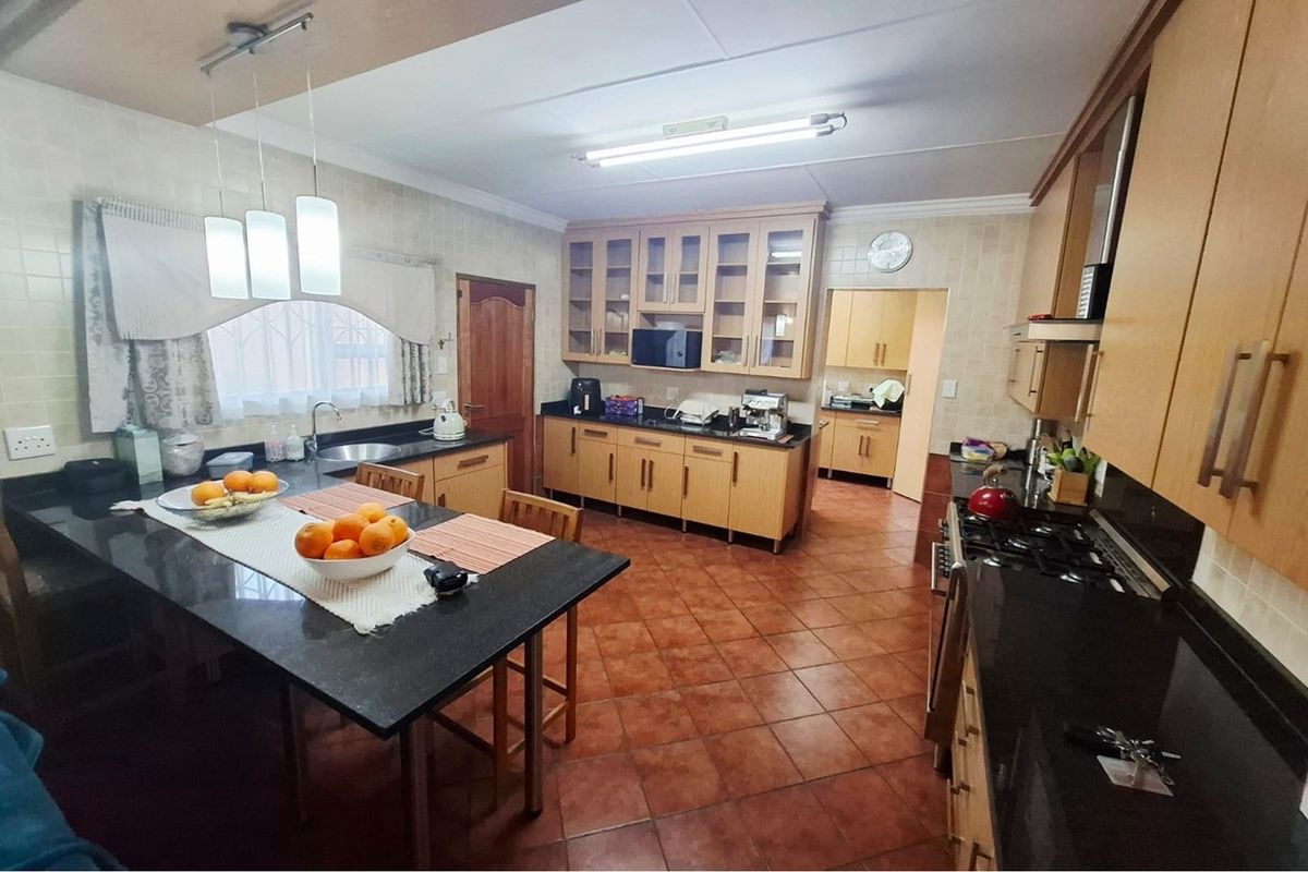 Spacious kitchen featuring granite countertops, extensive wooden cabinetry, gas hob, extractor fan, and a breakfast nook, with an adjoining scullery area.