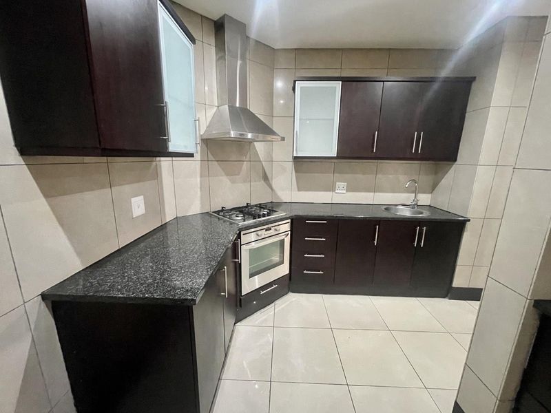 A modern kitchen featuring dark wood cabinetry, granite countertops, a built-in gas hob, oven, and stainless steel extractor fan with fully tiled finishes.