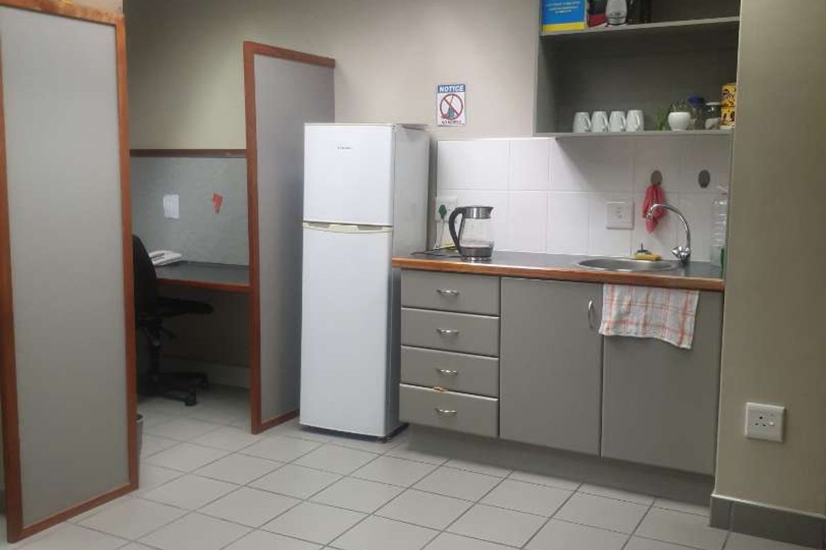 A functional industrial kitchenette area featuring built-in cabinetry, a stainless steel sink, tiled flooring, and a drop ceiling with integrated lighting.