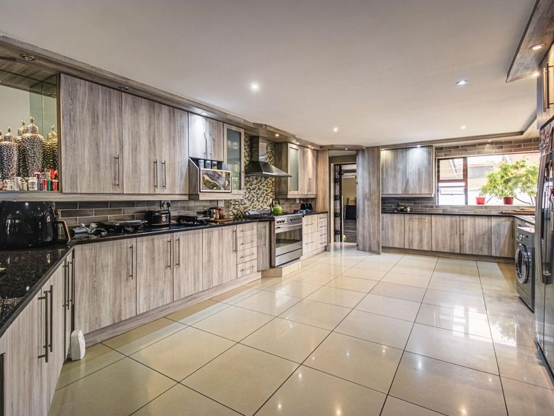 Spacious modern kitchen featuring wood-grain cabinetry, granite countertops, mosaic backsplash, and high-quality stainless steel appliances with ample floor space.