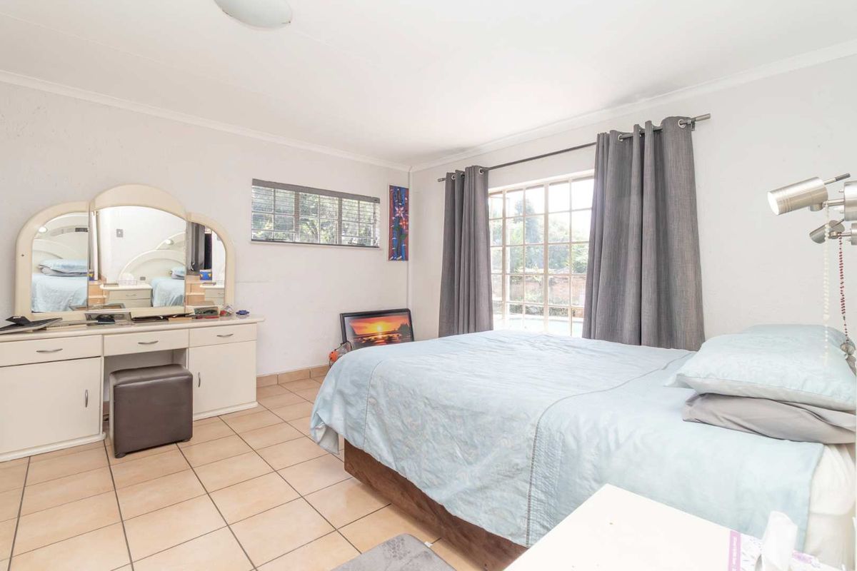 A bedroom featuring tiled flooring, large windows with curtain rails, and a neutral color palette, offering a functional and well-lit living space.