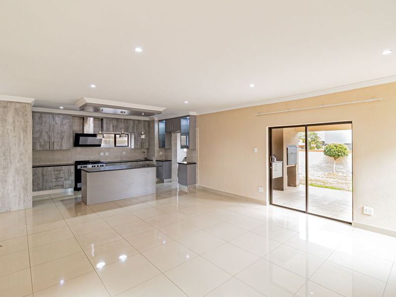 Spacious open-plan kitchen and living area featuring modern cabinetry, tiled floors, and direct access to a covered patio with a built-in braai.