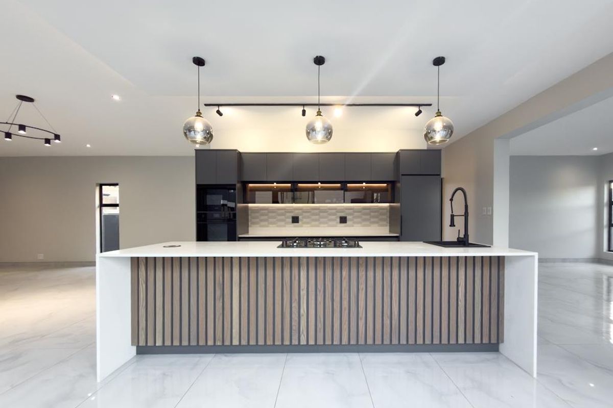 Modern open-plan kitchen featuring a large central island with stone countertop, integrated gas hob, sleek cabinetry, and contemporary pendant lighting.