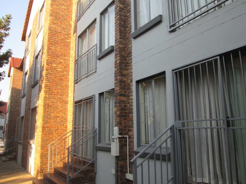 Exterior view of a multi-story apartment building featuring face-brick accents, metal security gates, and external staircases.