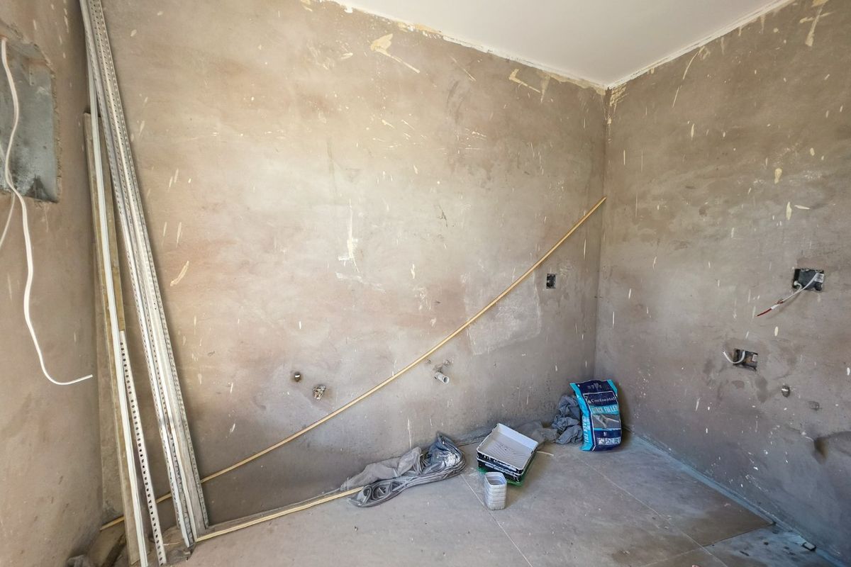 An unfinished kitchen space in shell condition, featuring exposed plaster walls, electrical rough-ins, and plumbing points ready for final installation and fit-out.