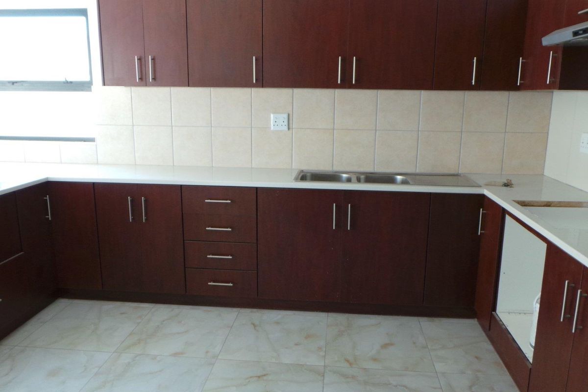 A functional kitchen featuring dark wood cabinetry, light-colored tiled backsplash, stone-look countertops, and a stainless steel double sink.