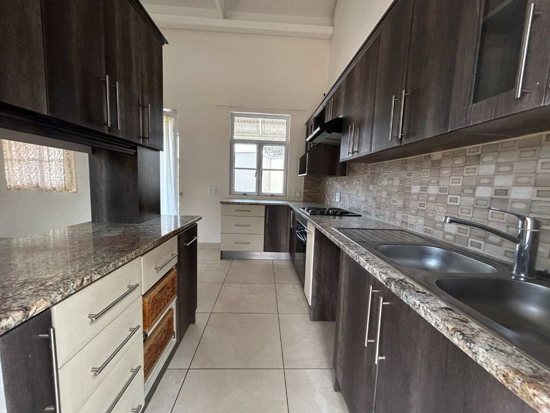 A functional kitchen featuring dark wood cabinetry, granite countertops, a double stainless steel sink, built-in oven, gas hob, and neutral tiled flooring.