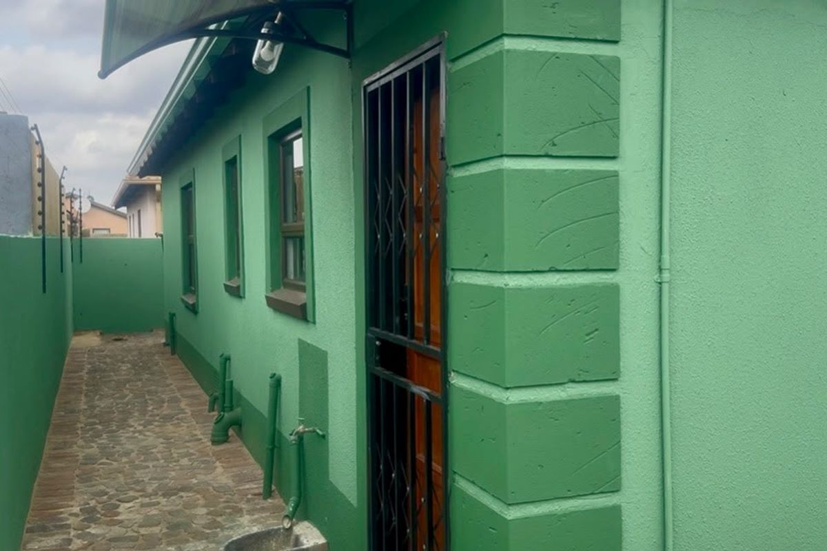 Side exterior view of the property featuring a stone paved walkway, security gate, and electric fencing along the perimeter wall.