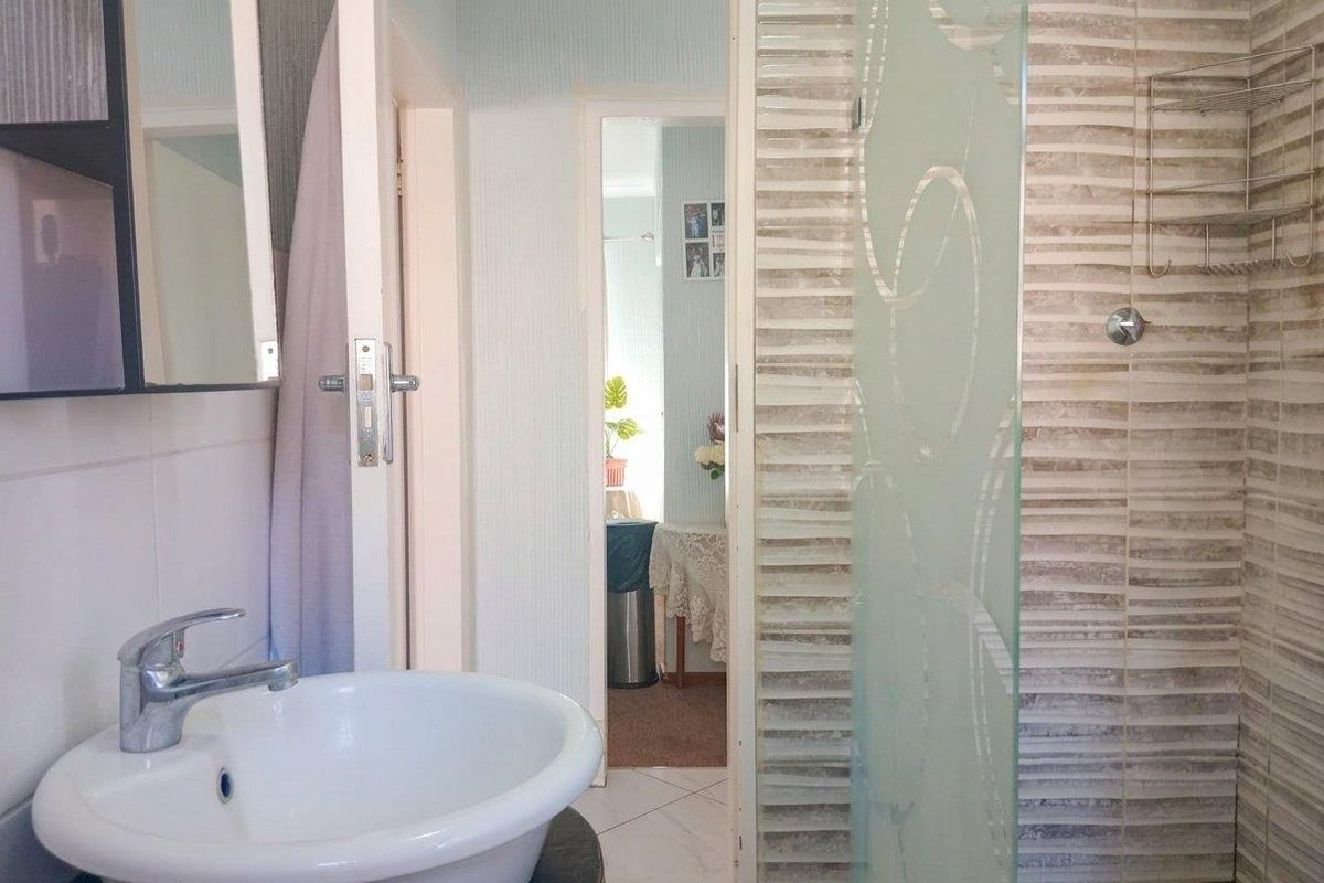 A functional bathroom featuring a basin with a mixer tap, a shower enclosure with decorative glass, and tiled wall finishes.