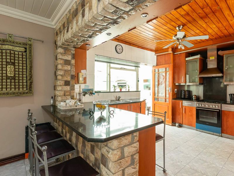 A rustic-style kitchen featuring a stone breakfast bar, timber ceiling, built-in oven, and ample cabinetry, offering a warm and functional cooking space.