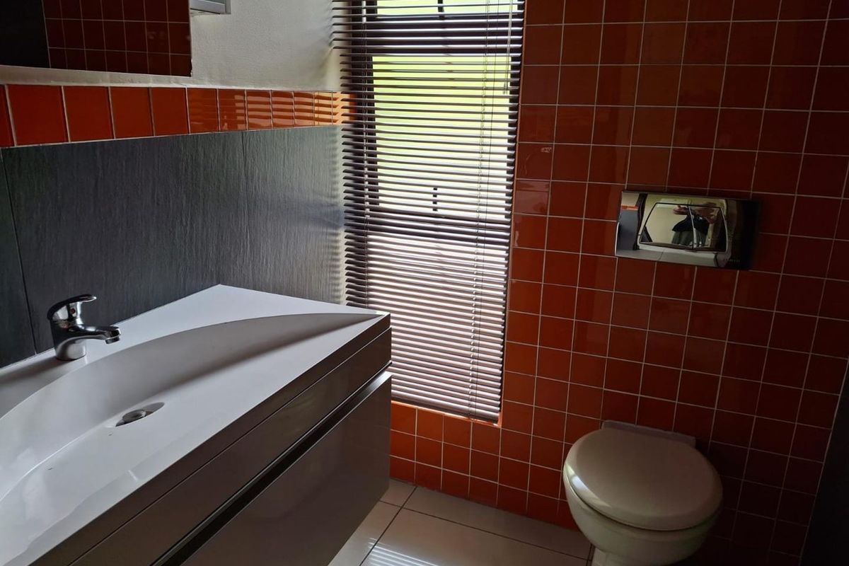 Modern bathroom featuring a wall-mounted vanity with basin, wall-hung toilet with concealed cistern, and vibrant orange tiled wall accents.