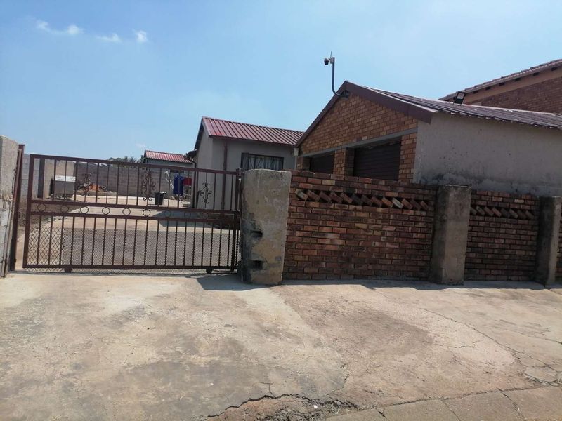 Front exterior view of the property featuring a concrete driveway, brick boundary wall, and metal sliding gate entrance.
