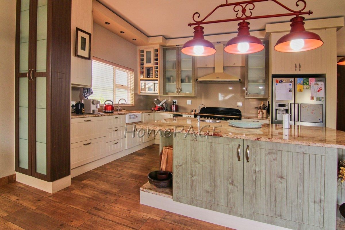 A well-appointed kitchen featuring a large central island, granite countertops, custom cabinetry, and integrated appliances with warm wood-look flooring.