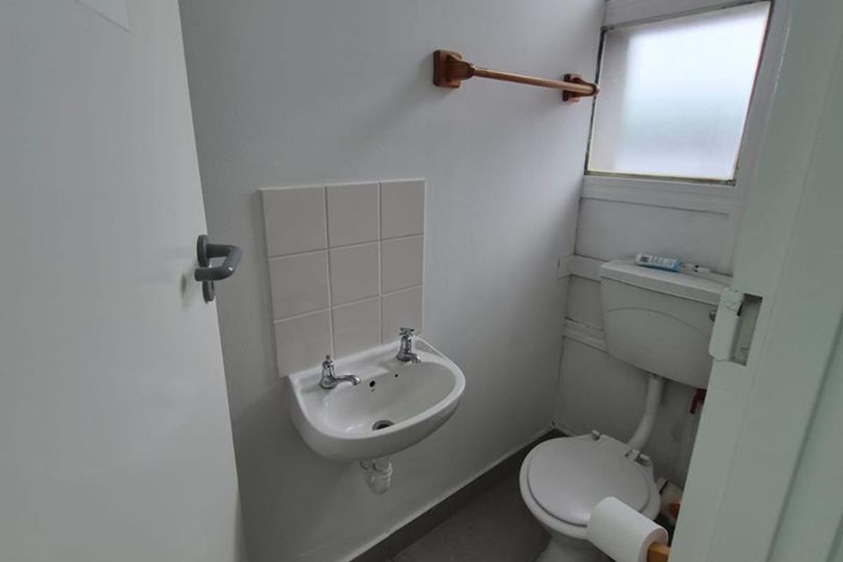 A compact office restroom featuring a wall-mounted basin, toilet, and tiled flooring with a frosted window for natural light.