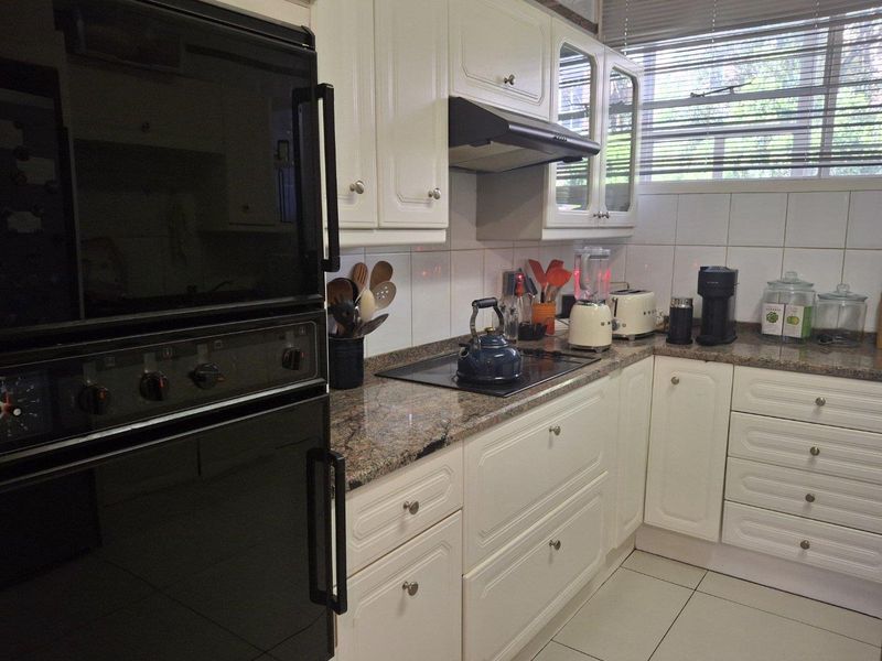 A functional kitchen featuring white cabinetry, granite countertops, a built-in oven, and a hob with an extractor fan.