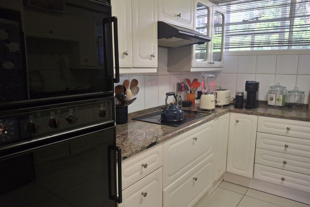 A functional kitchen featuring white cabinetry, granite countertops, a built-in oven, and a hob with an extractor fan.