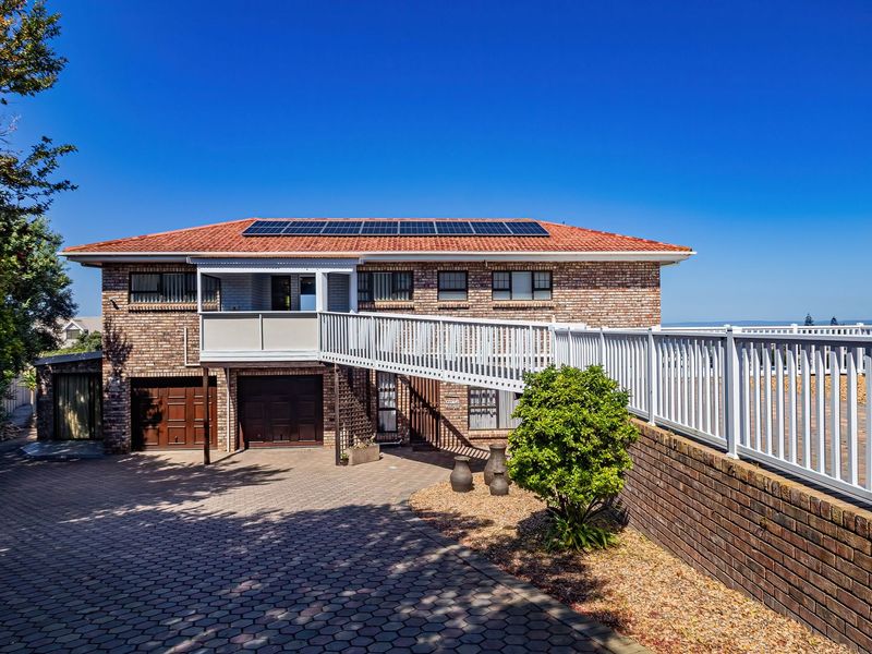 A well-maintained double-story brick house featuring a paved driveway, double garage, elevated balcony, and roof-mounted solar panels under a clear blue sky.