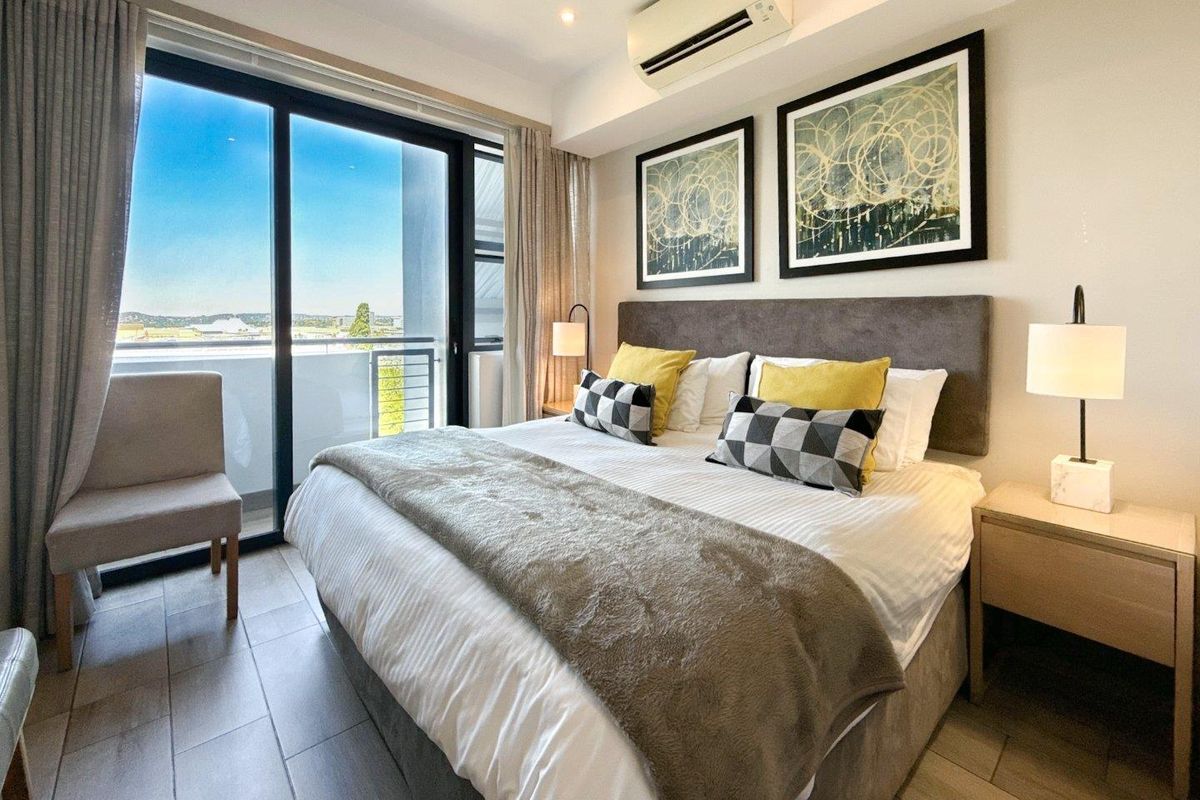 A well-maintained bedroom featuring tiled flooring, a wall-mounted air conditioning unit, and large sliding glass doors leading to a private balcony.