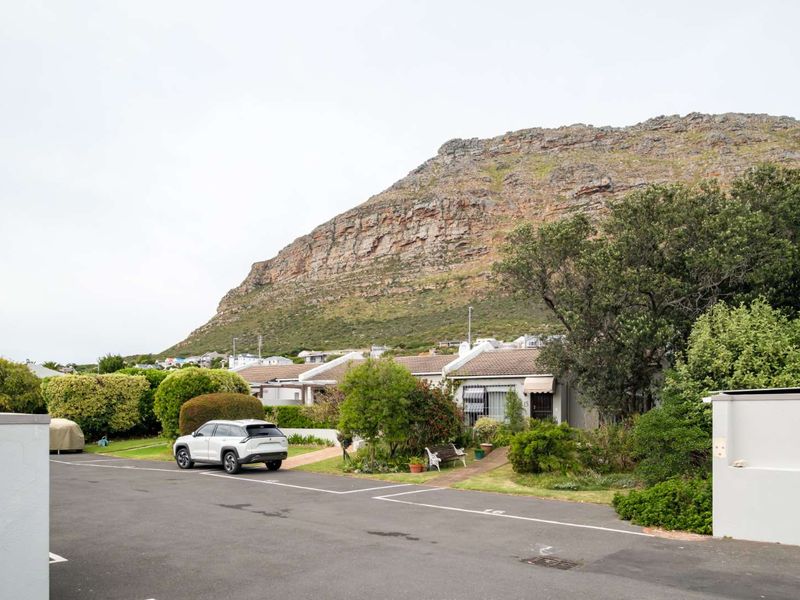 Front exterior view of a cluster home featuring a paved driveway, established garden, and a prominent mountain backdrop.