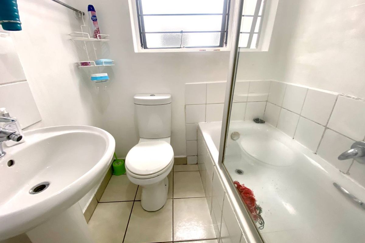 A functional bathroom featuring a pedestal basin, toilet, and a bathtub with a glass shower screen, finished with tiled flooring and wall splashbacks.