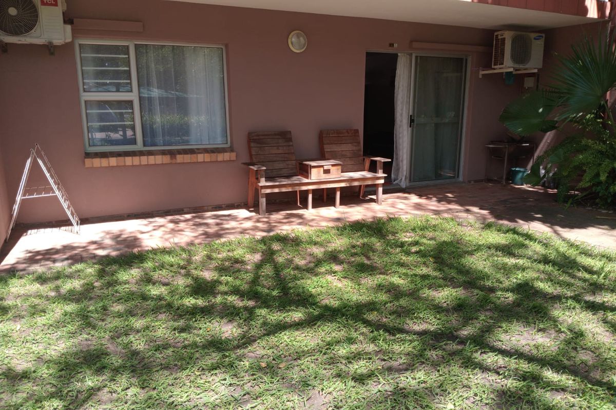 Rear exterior view of the townhouse featuring a paved patio area, small lawn, sliding door access, and wall-mounted air conditioning units.