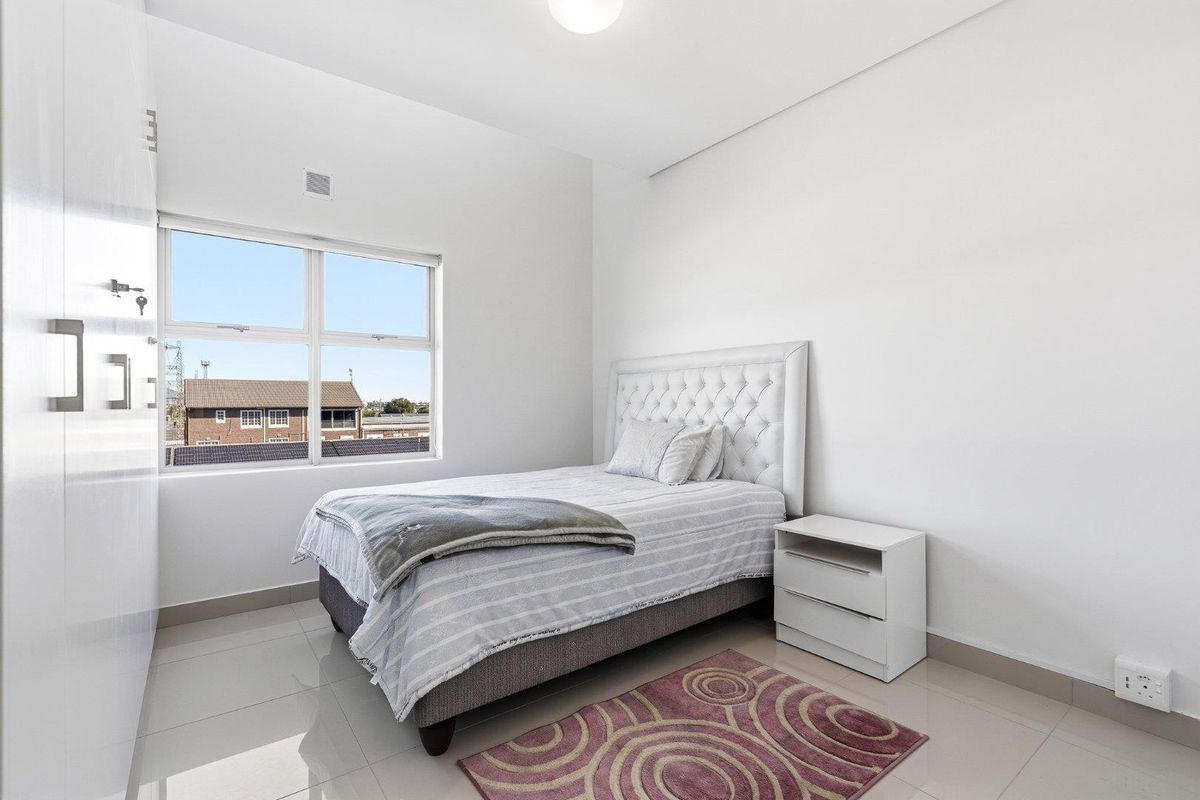 A bright, modern bedroom featuring neutral tiled flooring, a large window, and a built-in wardrobe, offering a clean and functional living space.
